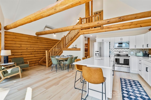 kitchen featuring log walls, a breakfast bar, white cabinets, light wood finished floors, and stainless steel appliances