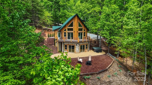 back of house featuring stone siding, a wooded view, and a deck