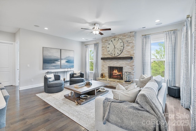 living room with ceiling fan, a stone fireplace, wood finished floors, baseboards, and recessed lighting
