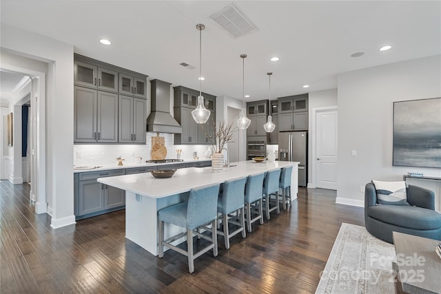 kitchen featuring gray cabinets, stainless steel appliances, wall chimney exhaust hood, and visible vents
