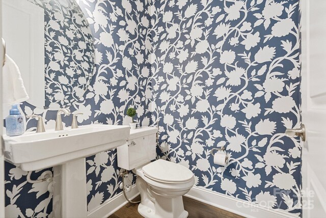 bathroom featuring toilet, wallpapered walls, and baseboards