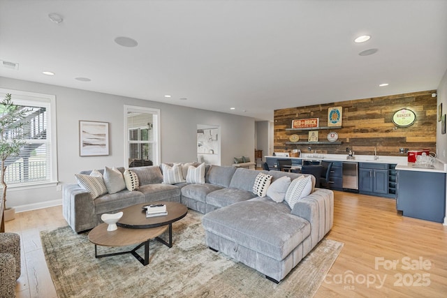 living room with indoor wet bar, recessed lighting, light wood finished floors, and wooden walls