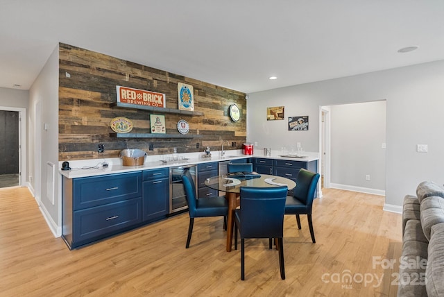 dining area with wooden walls, beverage cooler, wet bar, baseboards, and light wood-type flooring
