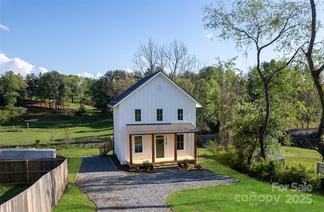 view of front of property with a front lawn, board and batten siding, fence, and covered porch
