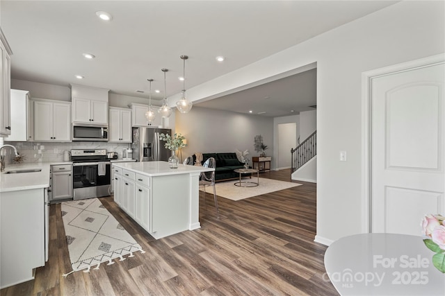 15622 Little Bluestem St, Charlotte, NC 28278 - kitchen featuring appliances with stainless steel finishes, a sink, a kitchen breakfast bar, light countertops, and dark wood finished floors