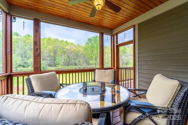 sunroom / solarium with ceiling fan, a wooded view, and outdoor dining space