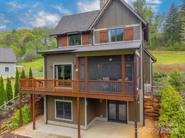 back of house featuring board and batten siding, a chimney, a wooden deck, a sunroom, and a patio area