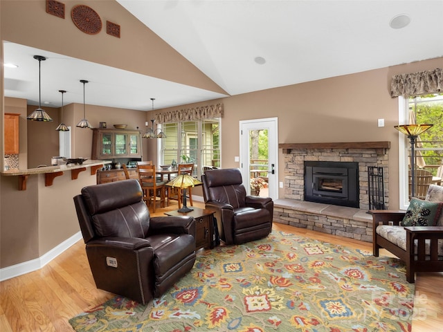 living room featuring a stone fireplace, baseboards, vaulted ceiling, and light wood-style floors