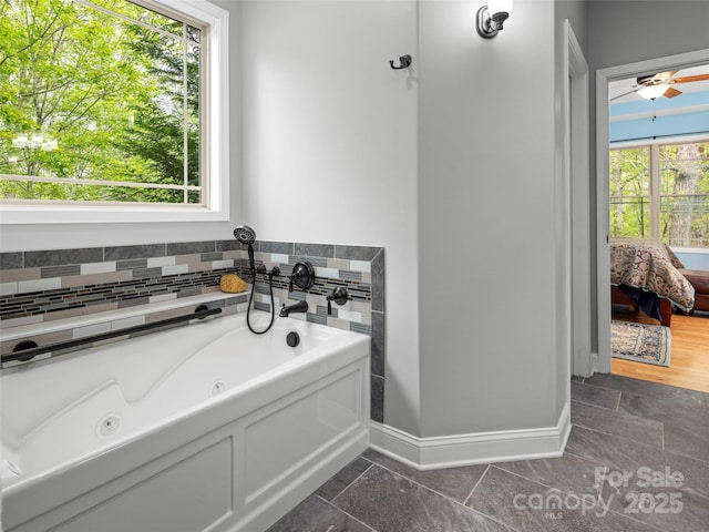 bathroom with a tub with jets, a healthy amount of sunlight, connected bathroom, and baseboards