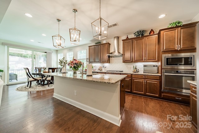 16507 Palisades Commons Dr, Charlotte, NC 28278 - kitchen featuring appliances with stainless steel finishes, wall chimney range hood, light stone counters, decorative light fixtures, and dark wood-style floors