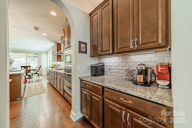 16507 Palisades Commons Dr, Charlotte, NC 28278 - kitchen with appliances with stainless steel finishes, arched walkways, decorative backsplash, light stone countertops, and wood finished floors