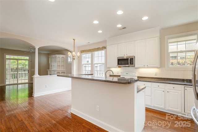 kitchen featuring visible vents, decorative columns, stove, stainless steel microwave, and arched walkways