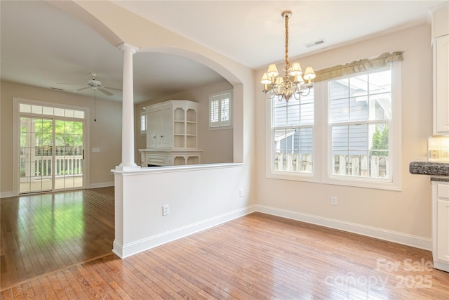 unfurnished dining area featuring visible vents, arched walkways, baseboards, ceiling fan with notable chandelier, and light wood-style floors