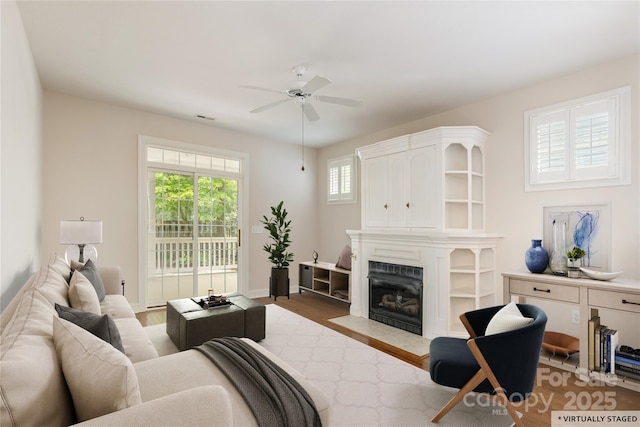 living area featuring ceiling fan, a fireplace with flush hearth, wood finished floors, and visible vents