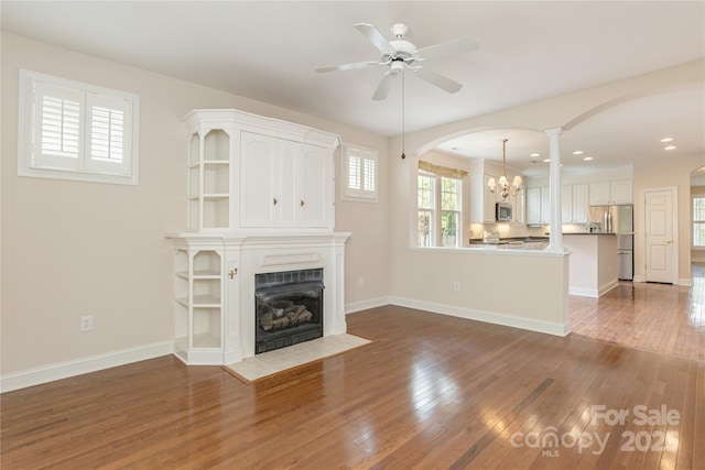 unfurnished living room featuring a ceiling fan, a fireplace with flush hearth, arched walkways, wood finished floors, and recessed lighting