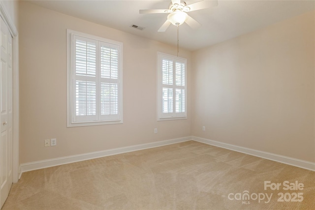 empty room with baseboards, visible vents, light carpet, and ceiling fan