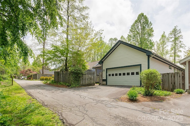 view of home's exterior featuring fence, an attached garage, and aphalt driveway