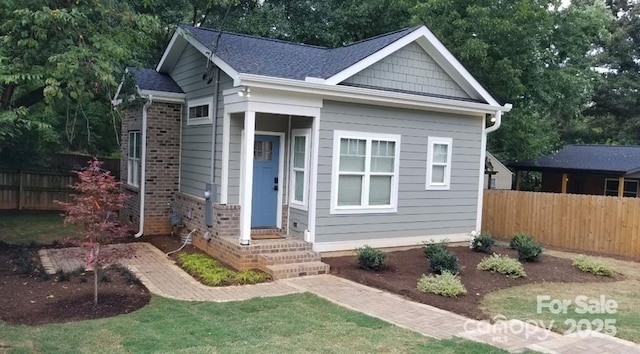 bungalow-style home featuring brick siding, a shingled roof, and fence