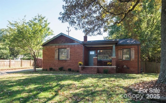 bungalow-style home featuring a chimney, brick siding, a fenced backyard, and a front lawn