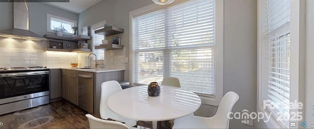 kitchen featuring tasteful backsplash, a sink, light countertops, wall chimney exhaust hood, and appliances with stainless steel finishes