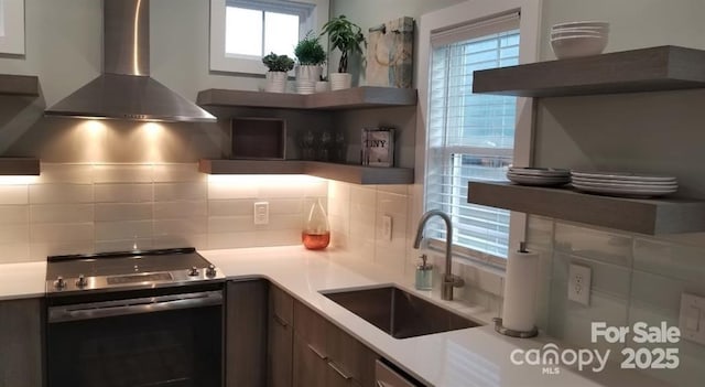 kitchen featuring decorative backsplash, wall chimney exhaust hood, stainless steel range with electric stovetop, and a sink