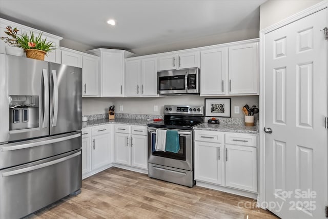 kitchen featuring white cabinets, stainless steel appliances, light stone countertops, and light wood-style flooring