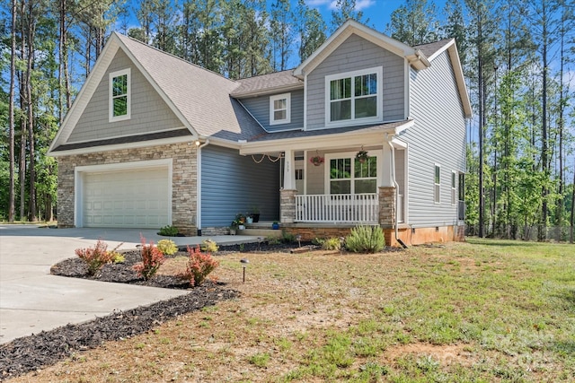 craftsman house featuring a front lawn, an attached garage, stone siding, concrete driveway, and a porch