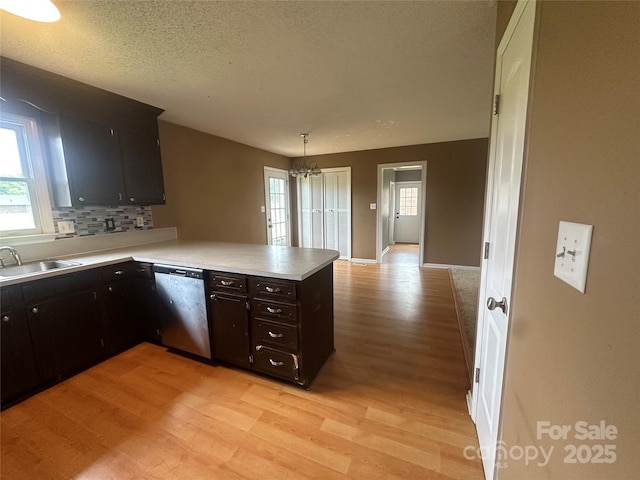 kitchen featuring light countertops, dishwasher, a sink, light wood-type flooring, and a peninsula