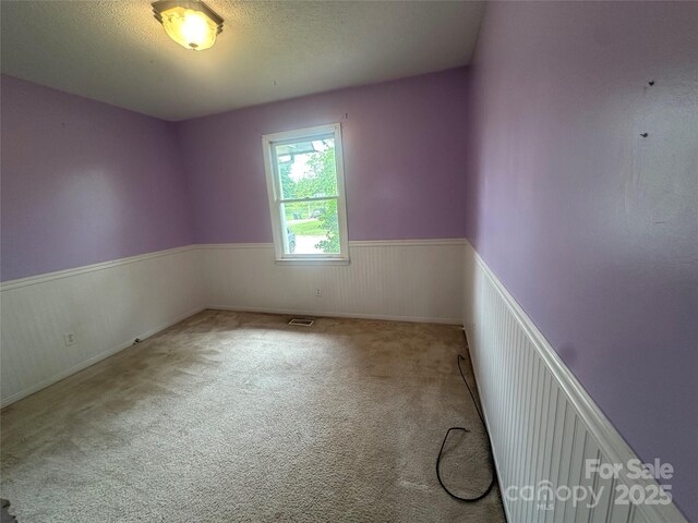 empty room featuring a wainscoted wall, visible vents, carpet floors, and a textured ceiling