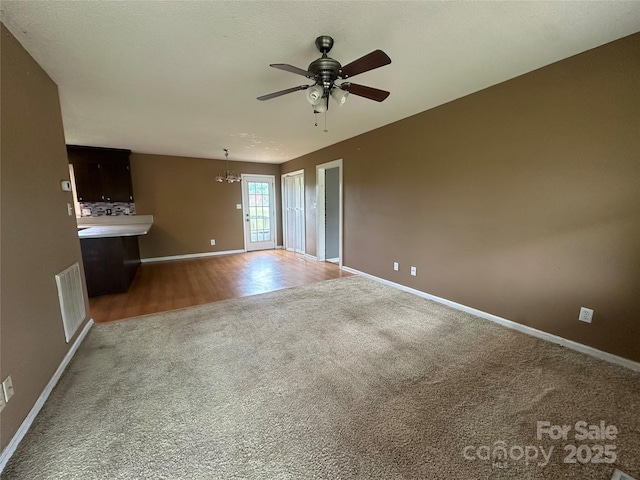 unfurnished living room featuring carpet flooring, visible vents, baseboards, wood finished floors, and ceiling fan with notable chandelier