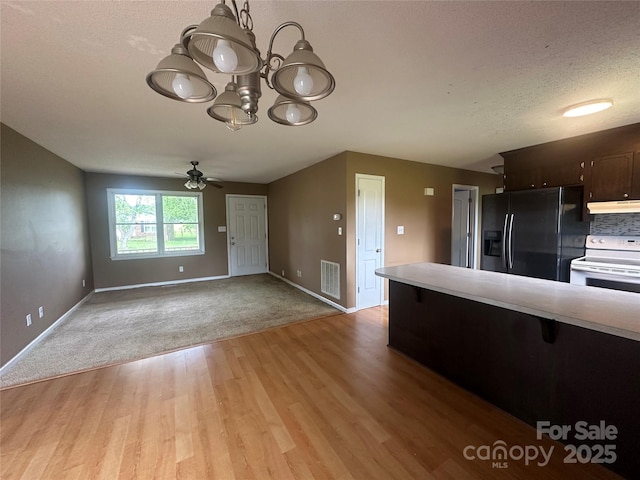 kitchen featuring electric stove, under cabinet range hood, light wood-style floors, black fridge, and light countertops