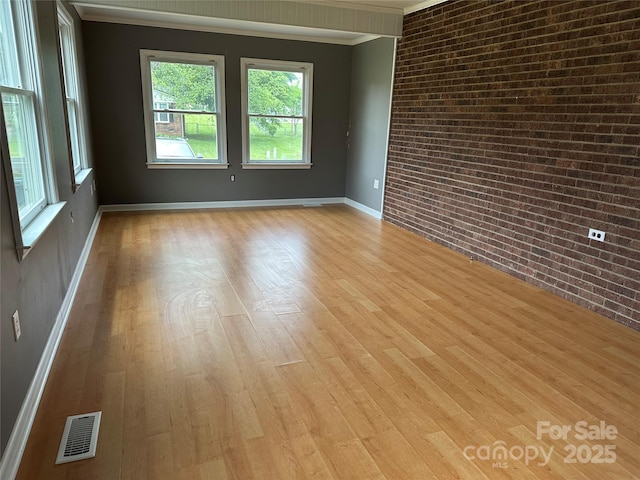 unfurnished room featuring visible vents, brick wall, crown molding, and light wood-style flooring