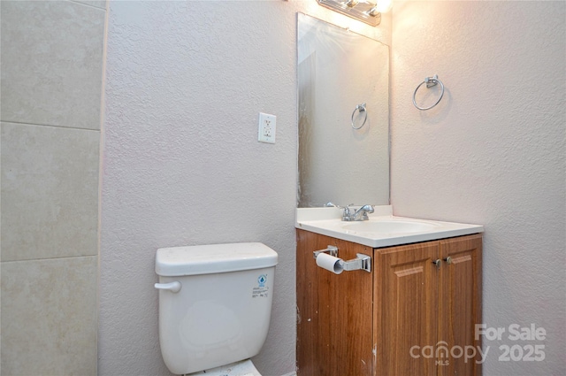 half bathroom with toilet, vanity, and a textured wall