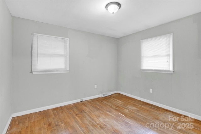 spare room with baseboards, wood finished floors, and visible vents