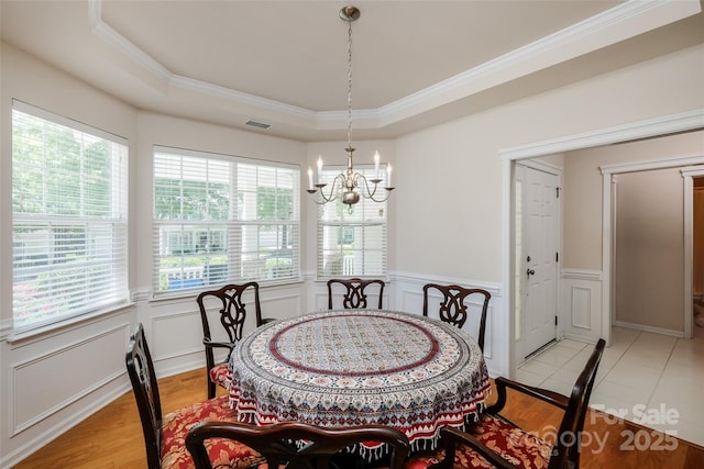 dining area with crown molding, a tray ceiling, an inviting chandelier, and a healthy amount of sunlight