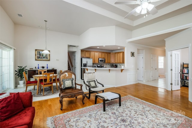 living room featuring visible vents, light wood-style flooring, ceiling fan, and a high ceiling