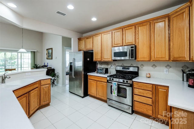 kitchen featuring brown cabinetry, a sink, appliances with stainless steel finishes, and light countertops