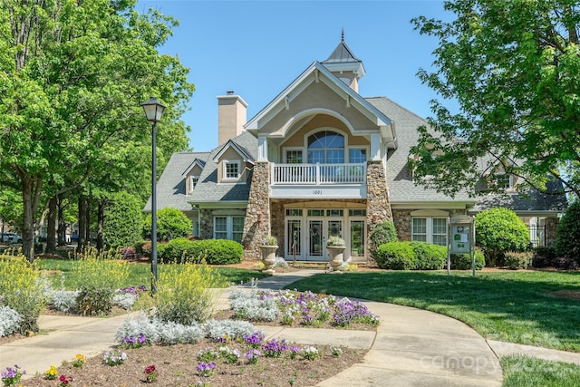 exterior space with a front lawn, stone siding, a chimney, a balcony, and french doors