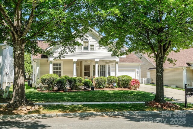view of front of house featuring a garage, covered porch, driveway, and a front yard