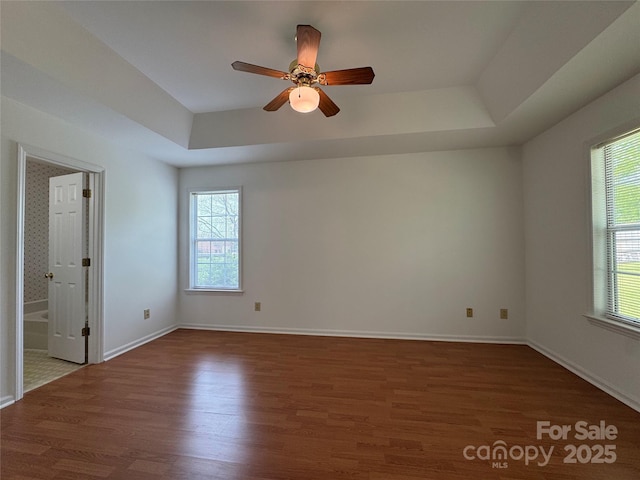 spare room with a ceiling fan, a healthy amount of sunlight, wood finished floors, and a tray ceiling
