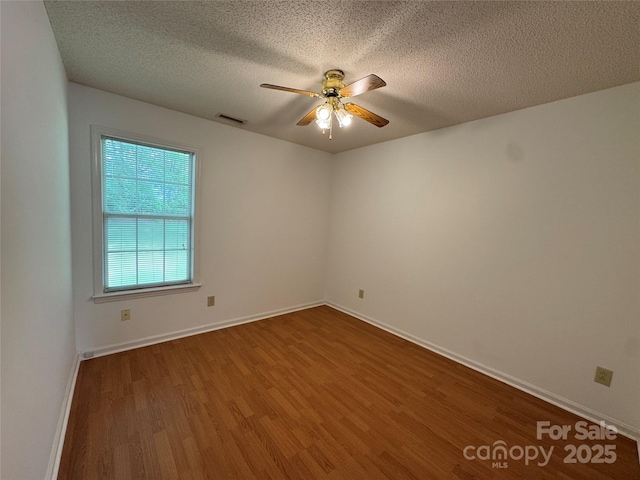 empty room with visible vents, wood finished floors, a ceiling fan, and a textured ceiling