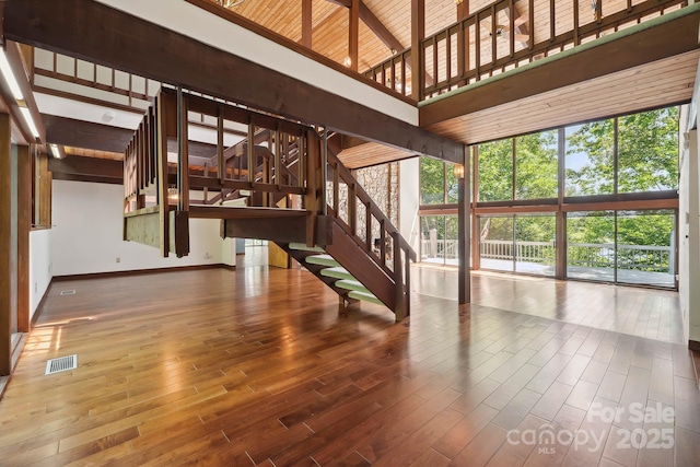 unfurnished living room featuring visible vents, a towering ceiling, wood finished floors, baseboards, and stairway