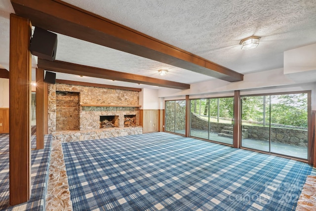 unfurnished living room featuring wooden walls, a textured ceiling, beam ceiling, and a wainscoted wall
