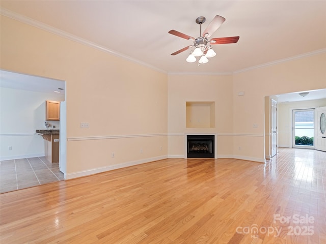 unfurnished living room featuring a fireplace, ceiling fan, ornamental molding, and light wood-type flooring