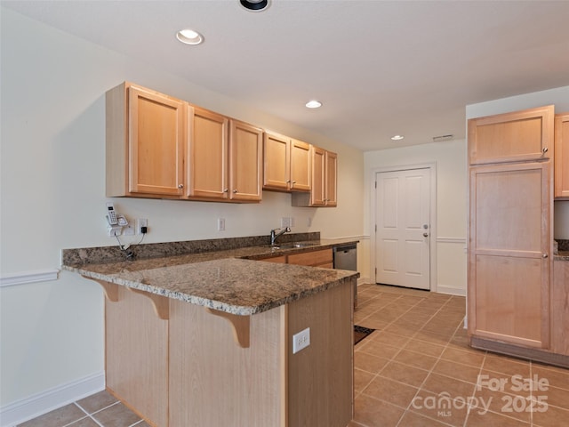 kitchen with a breakfast bar, a sink, light brown cabinets, a peninsula, and light tile patterned floors