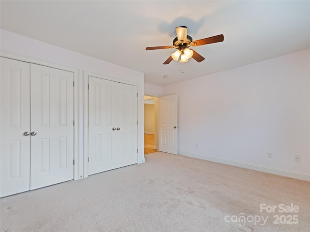 unfurnished bedroom featuring light colored carpet, multiple closets, ceiling fan, and baseboards