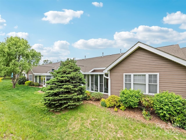 rear view of property with a lawn, roof with shingles, and a sunroom