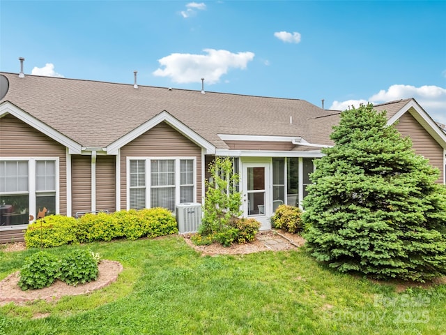 rear view of property with roof with shingles, central air condition unit, and a yard
