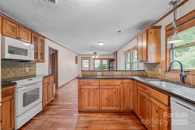 kitchen featuring light wood-type flooring, a sink, brown cabinetry, and white appliances