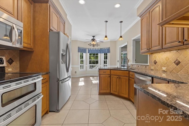 kitchen featuring a sink, stainless steel appliances, light tile patterned floors, brown cabinetry, and a ceiling fan